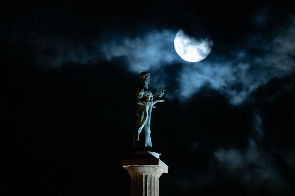 La gigantesca luna blu è parzialmente ostruita dalle nuvole in questa immagine lunatica che la mostra mentre si erge sopra un monumento a una persona in piedi su un alto palo.