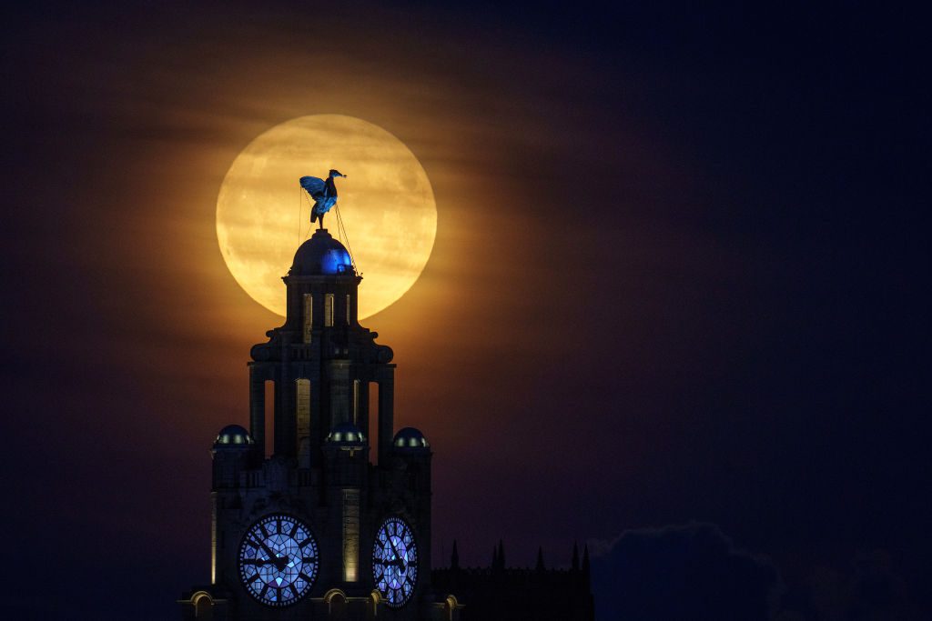 Una grande luna luminosa dietro un edificio sormontato da una grande statua di un uccello.