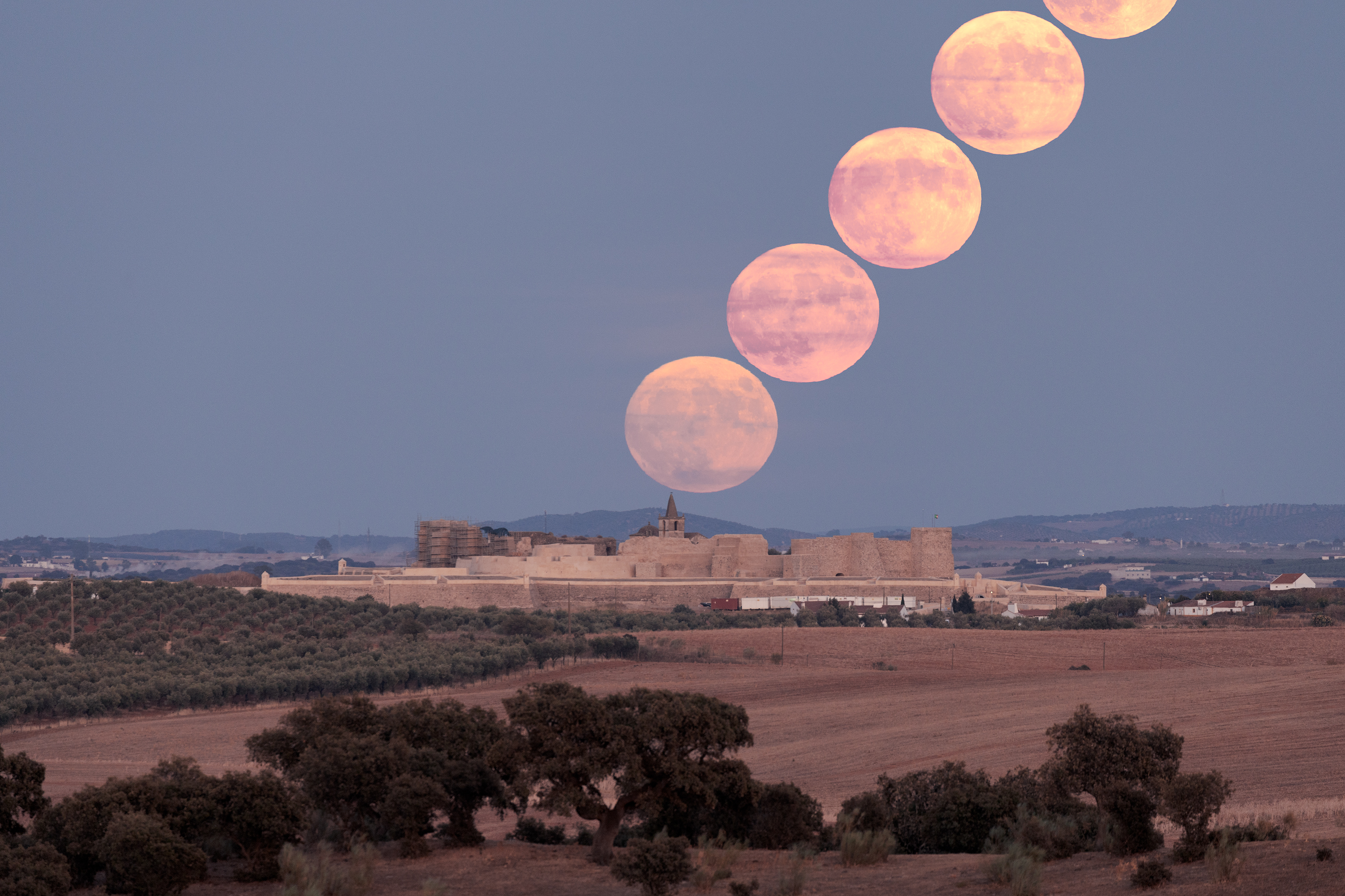 Una serie di cinque immagini time-lapse della super luna blu si alza nel cielo da un antico castello sottostante.