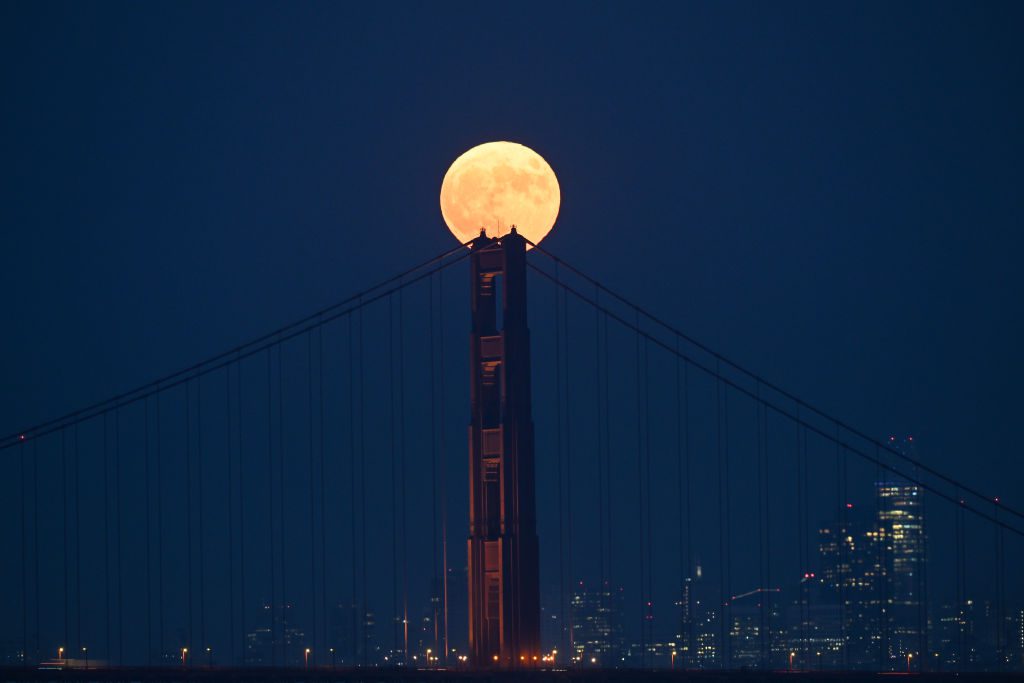 Una luminosa luna piena splende sopra il pilastro centrale del Golden Gate Bridge, con lo skyline della città sullo sfondo.