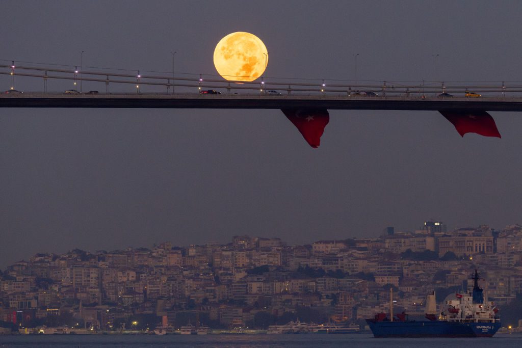 Le auto percorrono il ponte sospeso mentre la luna piena sorge sopra di loro.