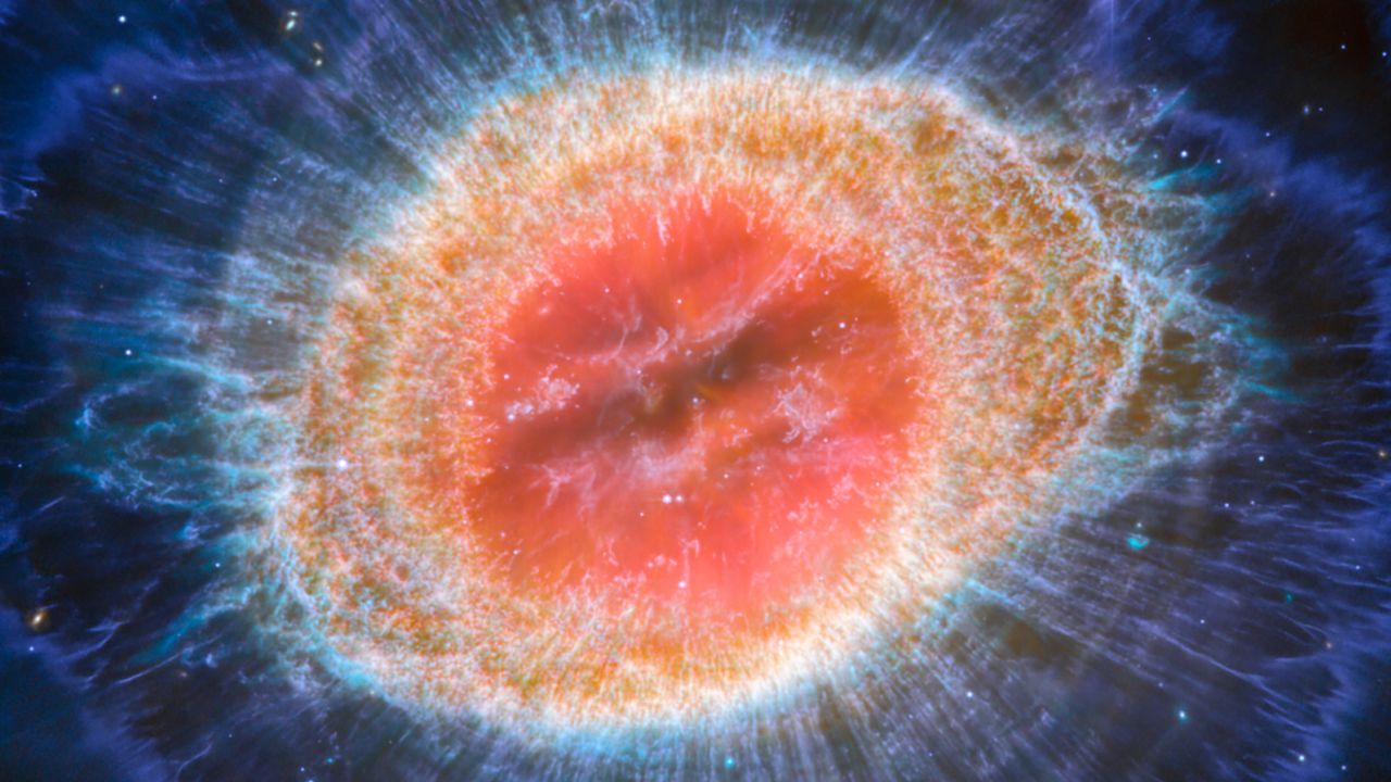 Il telescopio spaziale James Webb della NASA, dell'Agenzia spaziale europea e dell'Agenzia spaziale canadese ha osservato la famosa Nebulosa Anello con un dettaglio senza precedenti.  La Nebulosa Anello è costituita da una stella che perde i suoi strati esterni quando rimane senza carburante, ed è una tipica nebulosa planetaria.  Conosciute anche come M57 e NGC 6720, entrambe sono relativamente vicine alla Terra a circa 2.500 anni luce di distanza.  Questa nuova immagine fornisce una risoluzione spaziale e una sensibilità spettrale senza precedenti.  In particolare, il MIRI (strumento a medio infrarosso) di Webb rivela particolari dettagli nelle caratteristiche concentriche nelle regioni esterne delle nebulose ad anello (a destra).  Nella nebulosa ci sono circa 20.000 sfere dense, ricche di idrogeno molecolare.  Nella regione interna invece compaiono gas molto caldi.  Il guscio principale contiene un sottile anello ad emissione potenziata di molecole a base di carbonio note come idrocarburi policiclici aromatici (IPA).  Dietro il bordo esterno dell'anello principale si trovano circa dieci archi concentrici.  Si pensa che gli archi derivino dall'interazione della stella centrale con una compagna di piccola massa che orbita a una distanza simile a quella tra la Terra e il pianeta nano Plutone.  In questo modo, nebulose come la Nebulosa Anello rivelano una sorta di artefatto astronomico, poiché gli astronomi studiano la nebulosa per identificare la stella che l'ha creata. [Image description: This image of the Ring Nebula appears as a distorted doughnut. The nebula's inner cavity hosts shades of red and orange, while the detailed ring transitions through shades of yellow in the inner regions and blue/purple in the outer region. The ring's inner region has distinct filament elements.]