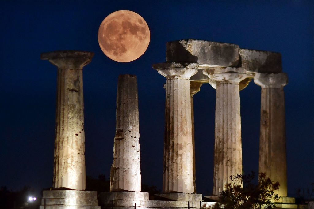 Luna blu gigante sopra cinque antiche strutture a pilastri.