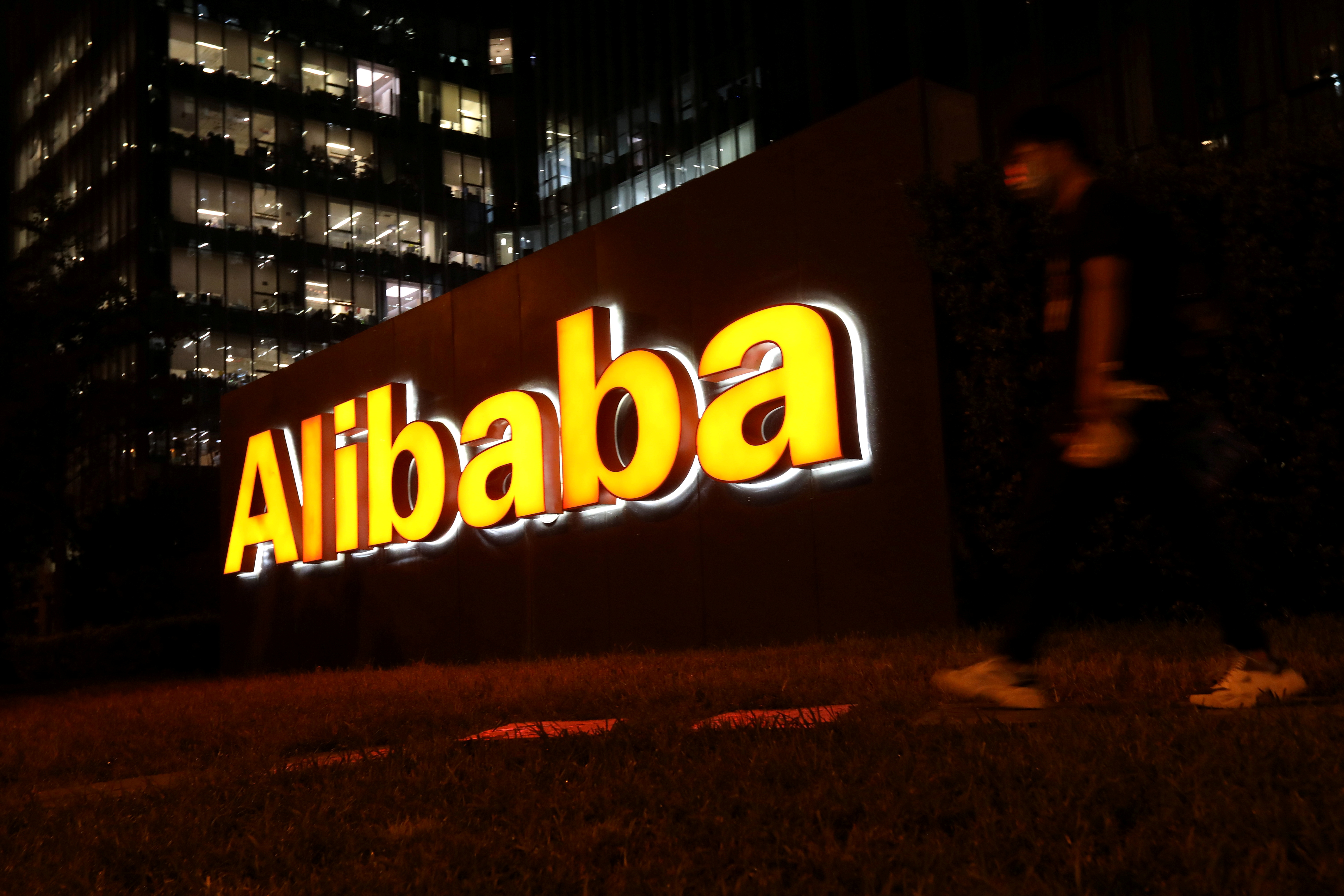 Un uomo cammina vicino al logo del Gruppo Alibaba nel suo edificio per uffici a Pechino