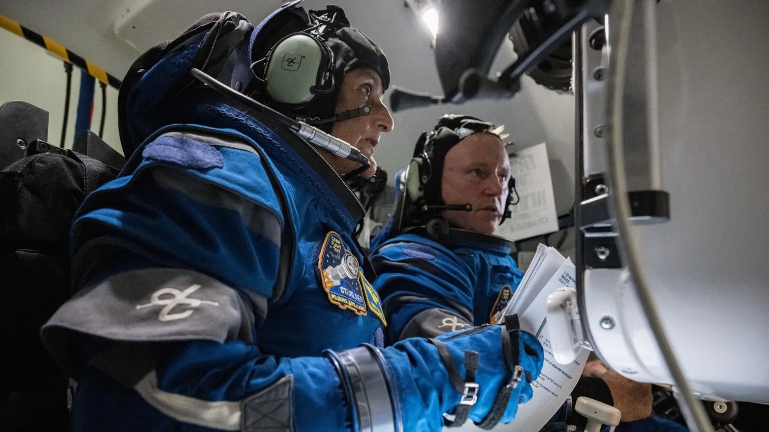Due astronauti che indossano tute spaziali guardano gli schermi di un simulatore